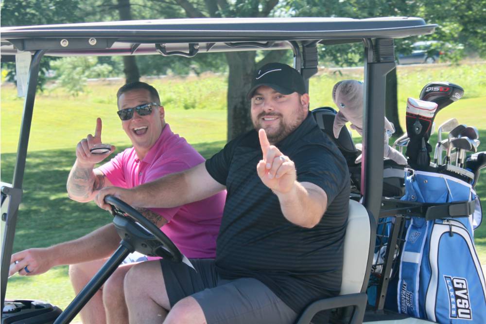 2 men hold up the number one on the golf cart